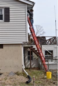 A man installing a ductless split cooling system on the side of a house in Lyme, CT.