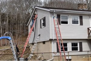 A man is installing ductless split cooling on the side of a house in Lyme,CT.